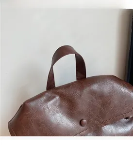Detail of soft brown leather backpack featuring a flat handle and vintage round button closure