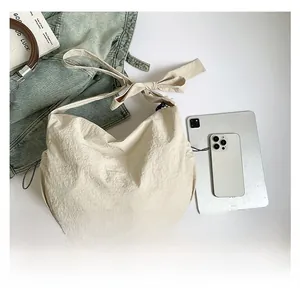Détail du sac croissant en nylon crème avec bandoulière nouée et accessoires lifestyle