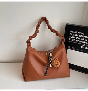 Détail d'un sac cabas caramel avec poignée froncée, texture cuir et breloque ourson