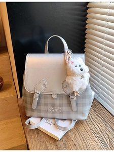 Gray checkered backpack with plush charm on a desk with notebooks and soft lighting