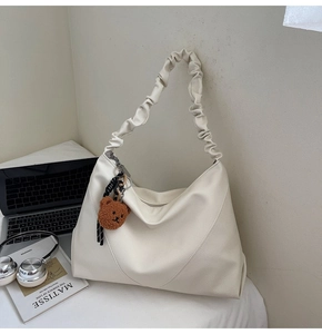Détail du sac cabas en cuir litchi blanc avec bandoulière plissée et charm d'ours