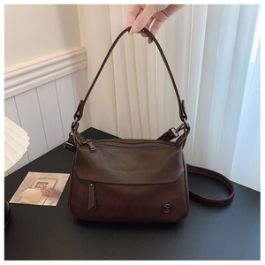 Macro detail of dark brown retro leather texture and circular metal logo on a crossbody bag