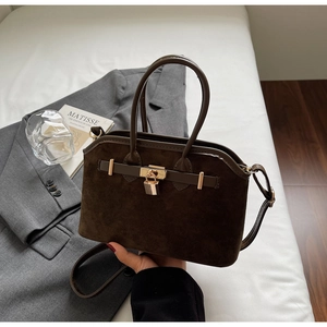 Gros plan d'un sac coquille en daim marron foncé avec détails dorés sur un lit blanc chic