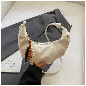 Détail du sac croissant crème avec poignée nouée et breloque en perles de bois vintage