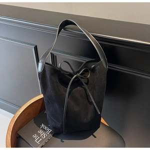Detail of minimalist black suede tote bag with drawstring bow and wide shoulder strap