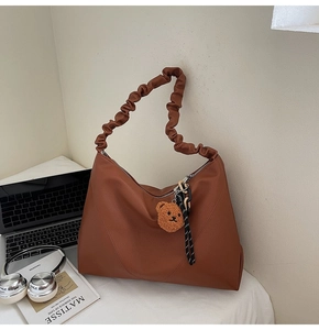 Détail du sac cabas marron à motif litchi avec bandoulière plissée et breloque ours
