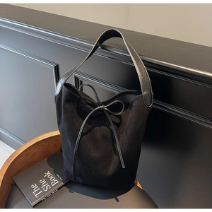 Detail of black suede tote bag featuring a decorative bow tie and wide leather strap