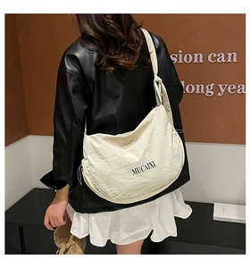 Détail d'un sac bandoulière croissant beige plissé avec logo MUCAIXI et large sangle nouée