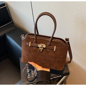 Détail du sac en daim marron avec cadenas doré et poignées en cuir élégantes
