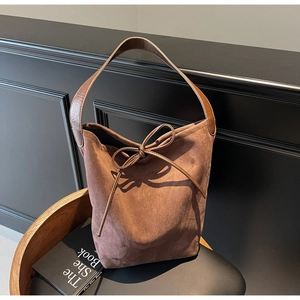 Detail of a brown suede bucket bag featuring bow drawstring closure and wide strap