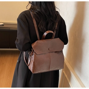 Rear view of model wearing dark brown faux leather backpack with top handle and flap cover