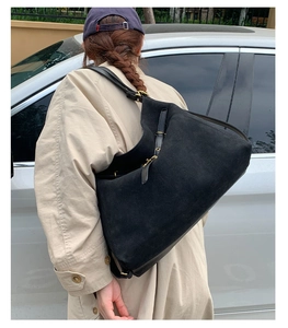 Detail of black suede hobo bag with gold metal buckle and adjustable strap on a trench coat