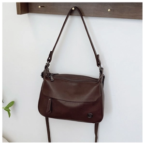 Detail of dark brown leather handbag featuring multi-zipper layers and a metallic logo