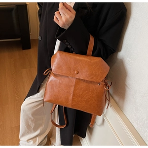 Close-up of vintage brown leather backpack featuring drawstring bow details and flap magnetic closure