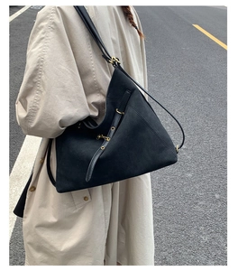 Detail of black suede large tote bag with crescent shape and brass buckle accents