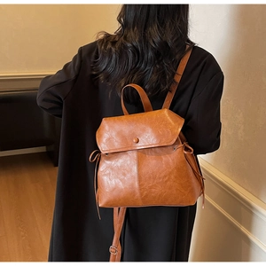 Rear view of model wearing a vintage brown backpack with flap closure and side drawstrings