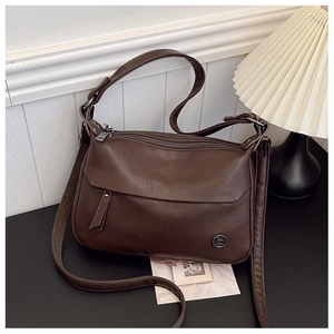 Detail of dark brown leather crossbody bag with multiple zippers and round metal logo