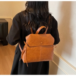 Detail of a brown vintage leather backpack featuring a round buckle and drawstring closure