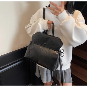 Detail of black leather backpack with side bow ties and round buckle on a model