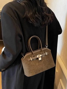 Sac hobo en daim marron avec boucle métallique porté à l'épaule par un mannequin