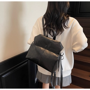 Detail of minimalist black leather backpack with flap design and side bow decoration