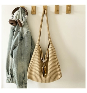 Detail of beige striped knit tote bag with wood bead charm on wall hook with lifestyle props
