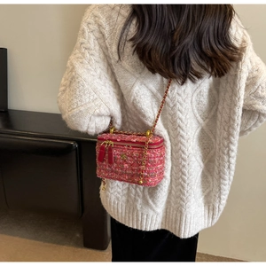 Pink tweed chain crossbody bag worn over a white cable knit sweater for winter style