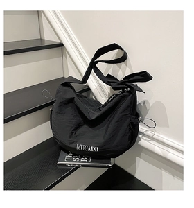 Détail du sac croissant en nylon avec bandoulière à nœud et texte sur l'escalier