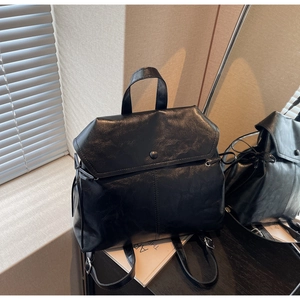 Detail of black faux leather backpack with metallic snap button and drawstrings