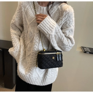 Detail of black tweed crossbody bag with gold floral logo worn on a white knit sweater
