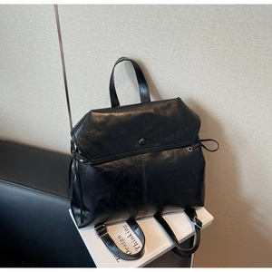 Detail of black faux leather backpack featuring oily texture and round buckle closure