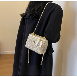Detail of tweed crossbody bag with golden flower clasp and woven chain strap worn by model