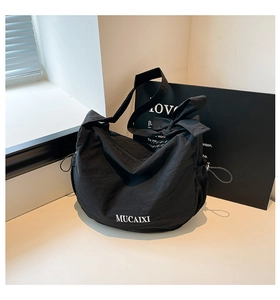 Détail du sac bandoulière noir avec lettrage logo, nœud d'épaule et texture nylon