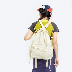 Detail view of beige drawstring backpack showing side pocket storing a badminton racket