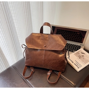 Detail of vintage brown leather backpack with drawstring and flap on a leather bench