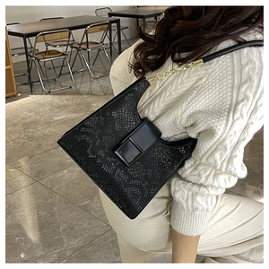 Detail of black snake pattern shoulder bag with gold chain strap on a white knit sweater
