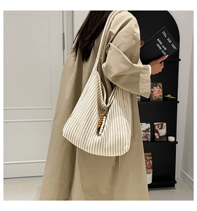Detail of knit tote bag featuring beige vertical stripes and a wooden bead charm
