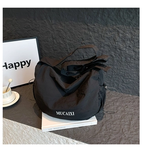 Détail du sac fourre-tout en nylon noir avec logo MUCAIXI sur fond gris texturé