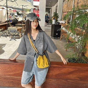 Close-up of bright yellow nylon bucket bag paired with a striped shirt and denim shorts