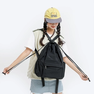 Model wearing a lightweight black nylon drawstring backpack with front zipper pocket