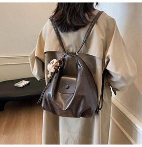 Detail view of a vintage dark brown leather backpack with plush pendant and flap closure