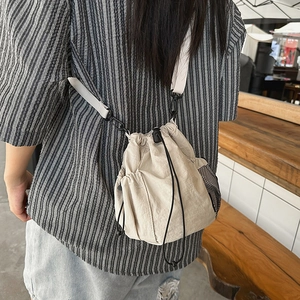 Detail of cream drawstring bucket bag showing mesh side pocket and nylon texture