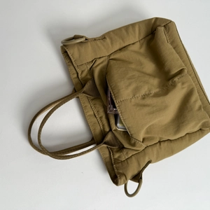 Detail of khaki nylon crossbody bag showing external pocket with everyday essentials