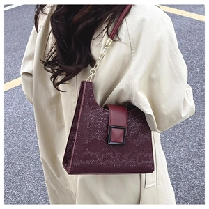 Detail of burgundy snakeskin texture handbag with gold chain strap on beige trench coat