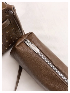 Detail of silver metal zipper and laser hollow design on brown litchi grain tote bag