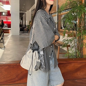 Detail of off-white nylon drawstring crossbody bag styled with striped shirt and denim shorts