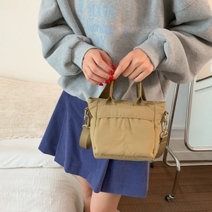 Detail showing khaki nylon crossbody bag with dual handles and detachable woven strap