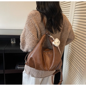Detail of a brown slouchy faux leather tote bag with a white plush bear charm accessory