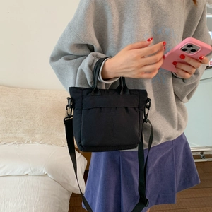 Detail of a black nylon crossbody phone bag showing the front pocket and adjustable strap