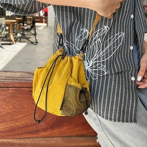 Detail of yellow nylon drawstring bucket bag with black mesh side pocket and strap